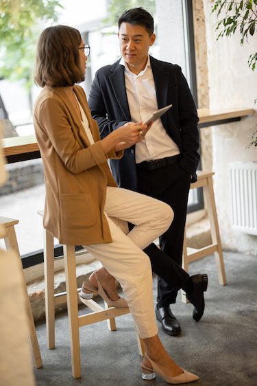 Businesswoman showing something on digital tablet to asian businessman in cafe or restaurant. Concept of remote and freelance work. Young caucasian girl wearing glasses. Idea of business cooperation